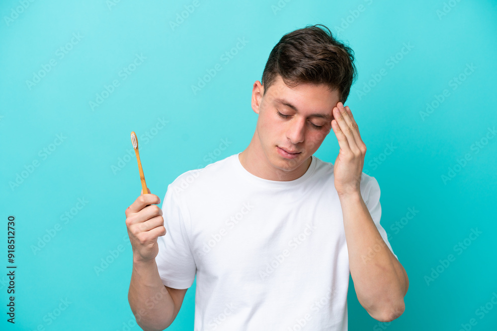 Young Brazilian man brushing teeth isolated on blue background with headache Young Brazilian man brushing teeth isolated on blue background with headache