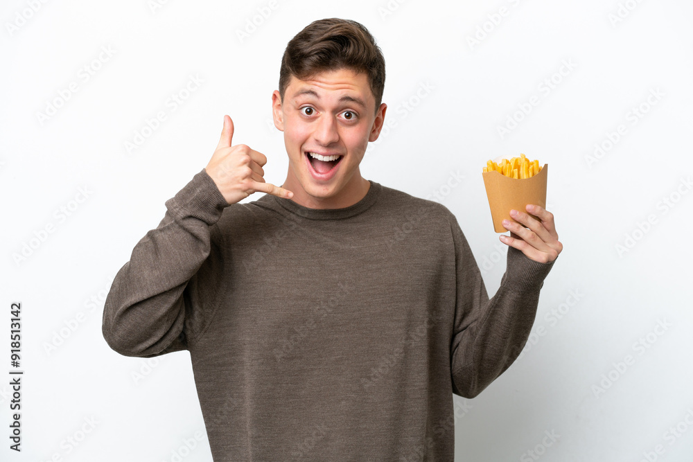 Young Brazilian man holding fried chips isolated on white background making phone gesture. Call me back sign Young Brazilian man holding fried chips isolated on white background making phone gesture. Call me back sign