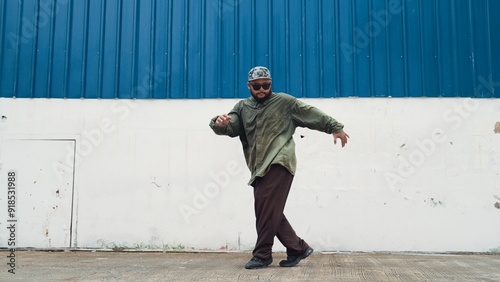 Hipster dancing b-boy foot step at street with blue wall. Asian break dancer practice street dance while stretch arms. Hip hop choreographer perform energetic dance. Outdoor sport 2024. Hiphop.