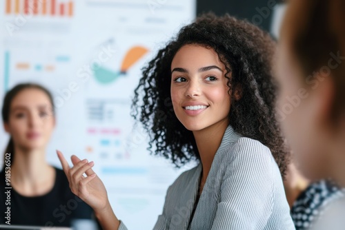 young businesswoman contributing to a team meeting with a chart-filled whiteboard in background