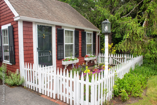Lovely summertime scene on Cape Cod. Small red cottage with decorative window flower boxes, white picket fence, and colorful garden of perennial flowers.