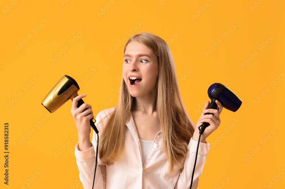 Surprised young blonde woman in pajamas with hair dryers on yellow background Surprised young blonde woman in pajamas with hair dryers on yellow background