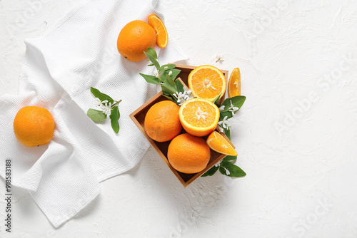 Wooden box of oranges with blooming branch on white table