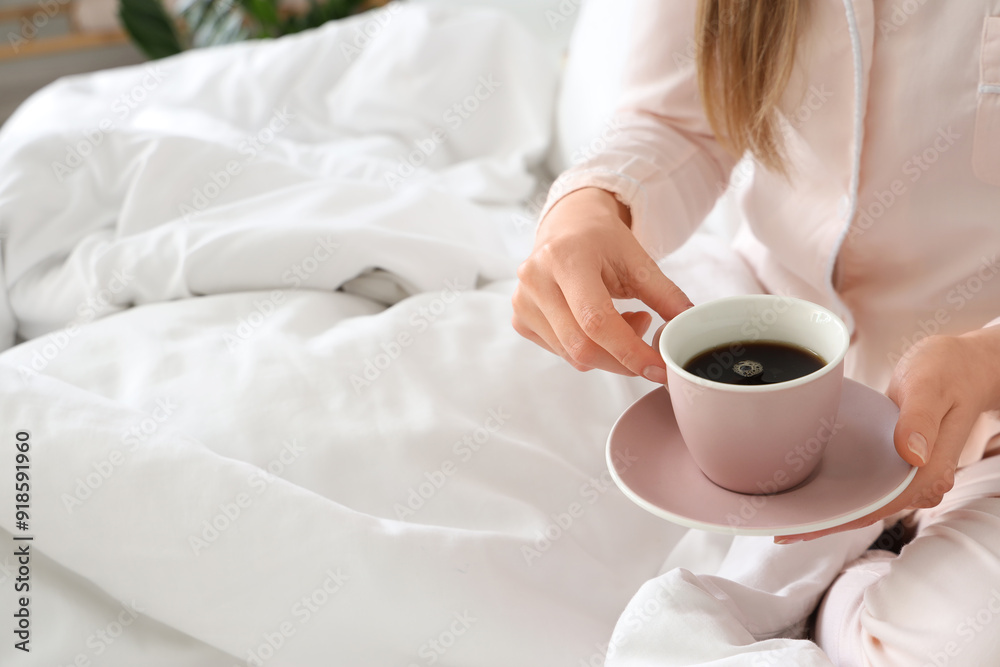 Woman holding cup of delicious coffee and saucer in bed