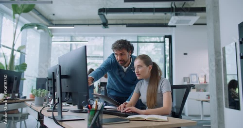 Attractive Caucasian leader controlling quality of work of his employee. Man comparing information on clipboard with data on computer. Busy woman typing text on keyboard while speaking with boss.