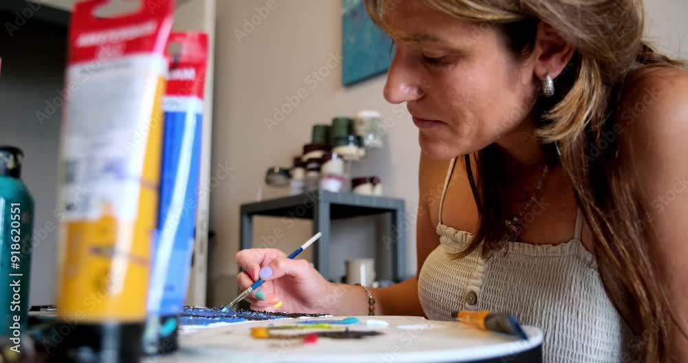 A close-up of a female painter demonstrating her craftsmanship as she works on a canvas with various colors of paint and brushes A close-up of a female painter demonstrating her craftsmanship as she works on a canvas with various colors of paint and brushes