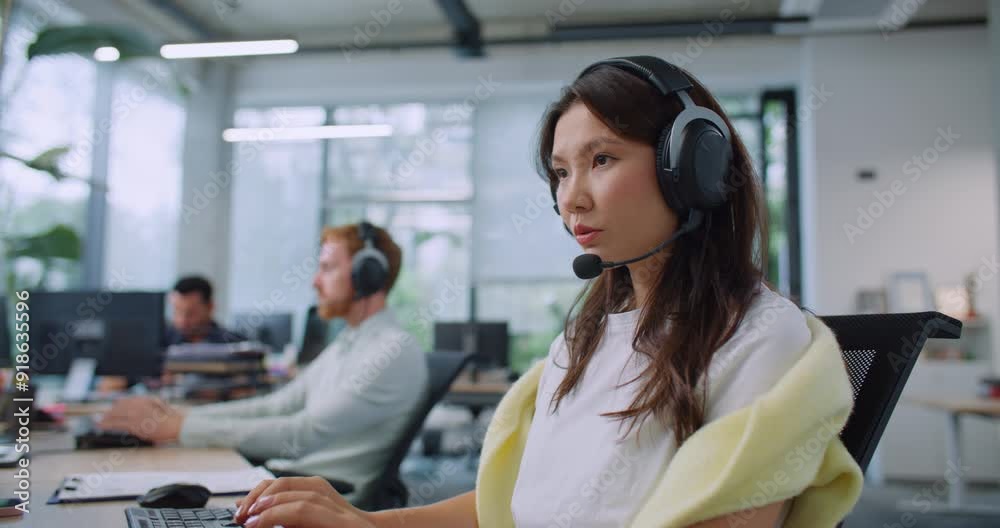 Side view of hardworking operators using headsets while consulting customers from office. Workers sitting at computer and entering information on keyboard. Providing support for clients. Side view of hardworking operators using headsets while consulting customers from office. Workers sitting at computer and entering information on keyboard. Providing support for clients.