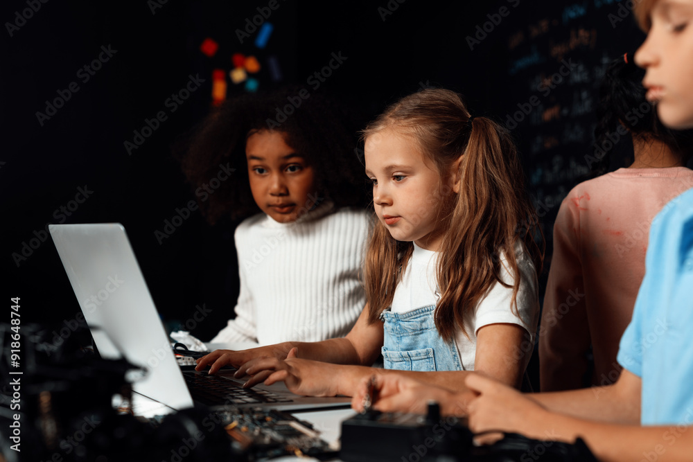 Smart girl in white bib learning about coding robotics technology using laptop in the STEM class. Schoolboy in blue shirt try to educate motherboard while smart schoolgirls reading code. Erudition. Smart girl in white bib learning about coding robotics technology using laptop in the STEM class. Schoolboy in blue shirt try to educate motherboard while smart schoolgirls reading code. Erudition.