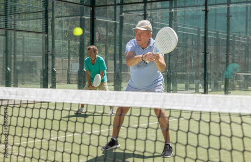 Elderly man and adult man in doubles playing paddle tennis on tennis court photo