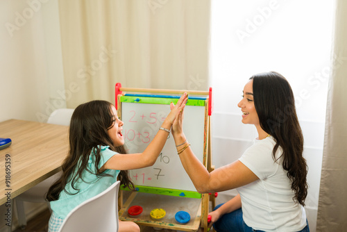 Latin mother giving her daughter a high five after completing a math lesson on a whiteboard while homeschooling her