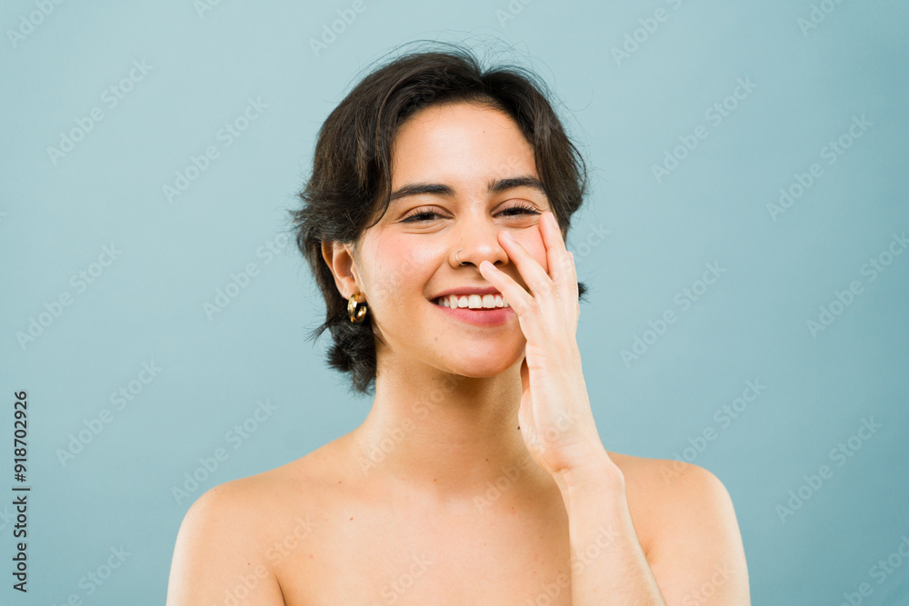 Beautiful young woman with short hair, smiling and touching her face on a blue background in a portrait Beautiful young woman with short hair, smiling and touching her face on a blue background in a portrait