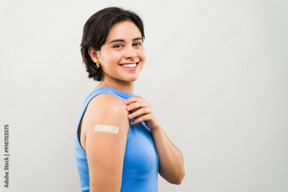 Happy, confident young woman smiles brightly after getting a vaccine in a studio. The bandage on her arm shows her commitment to health and prevention Happy, confident young woman smiles brightly after getting a vaccine in a studio. The bandage on her arm shows her commitment to health and prevention