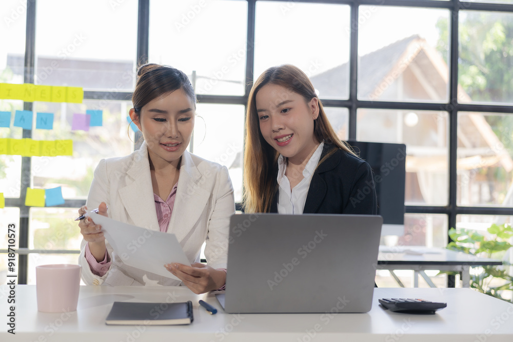 Two Asian businesswomen working together, meeting and discussing a new business project, creative team analyzing documents on marketing plan Laptop and documents on the table Two Asian businesswomen working together, meeting and discussing a new business project, creative team analyzing documents on marketing plan Laptop and documents on the table