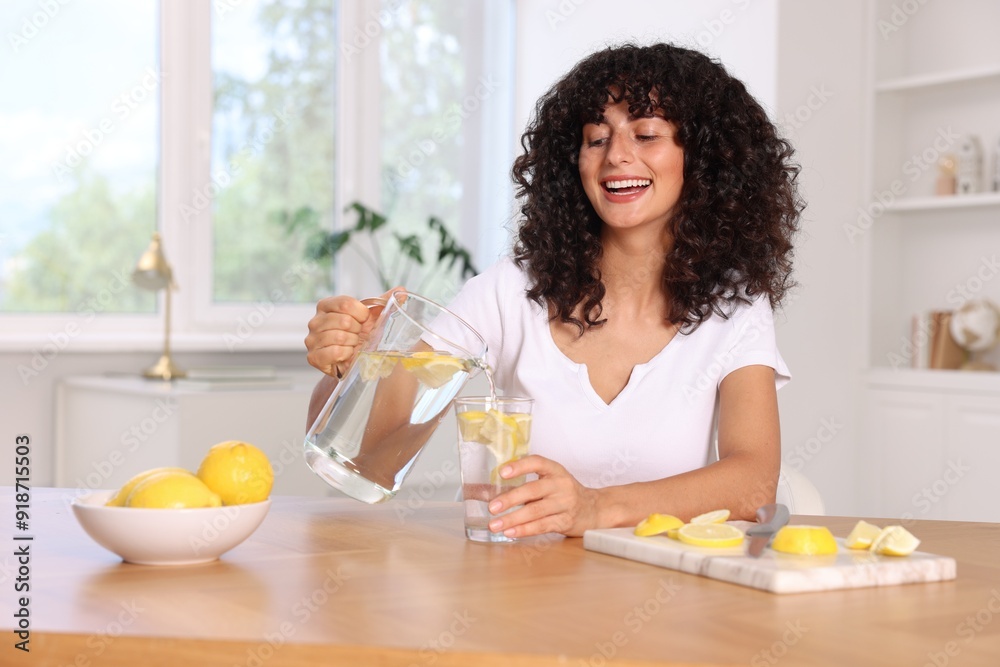 Woman pouring lemon water from jug into glass at table indoors Woman pouring lemon water from jug into glass at table indoors