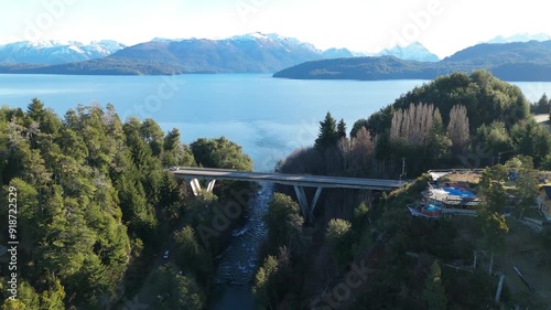 An aerial view capturing a scenic bridge crossing over a serene lake, surrounded by lush forests and towering mountains.  Bridge on the Correntoso River- Villa La angostura - Neuquen - Patagonia  photo