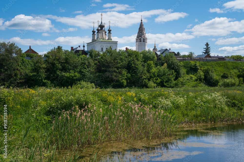 View of the Church of the Ascension of the Lord with a bell tower in the Alexander Monastery on the banks of the Kamenka River on a sunny summer day, Suzdal, Vladimir region, Russia View of the Church of the Ascension of the Lord with a bell tower in the Alexander Monastery on the banks of the Kamenka River on a sunny summer day, Suzdal, Vladimir region, Russia