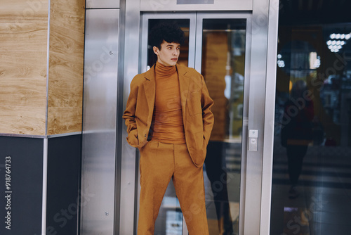 Stylish young man posing in a modern elevator, wearing a coordinated brown outfit that blends with the contemporary surroundings