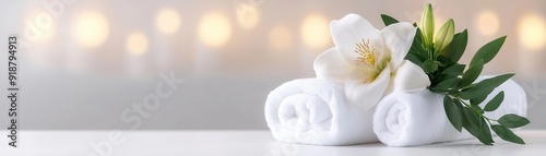 Elegant arrangement of white towels adorned with a flower and leaves, perfect for spa or wellness imagery.
