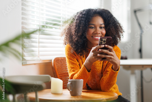 Принти на полотні Woman with afro hair, holding smartphone with coffee cup in hand stay connected online