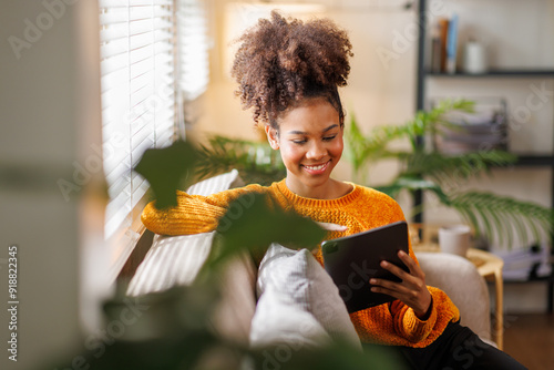 Happy young African American woman using tablet pc on sofa at home. Afro haired woman indoor. photo