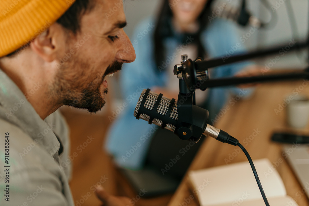 People in the podcast studio talking and recording. Focus on a smiling man with a yellow cap People in the podcast studio talking and recording. Focus on a smiling man with a yellow cap