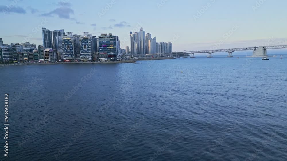 Smooth video shot from a drone, flying over the water, with skyscrapers as a backdrop, at sunset on Gwangalli Beach in Busan. Smooth video shot from a drone, flying over the water, with skyscrapers as a backdrop, at sunset on Gwangalli Beach in Busan.