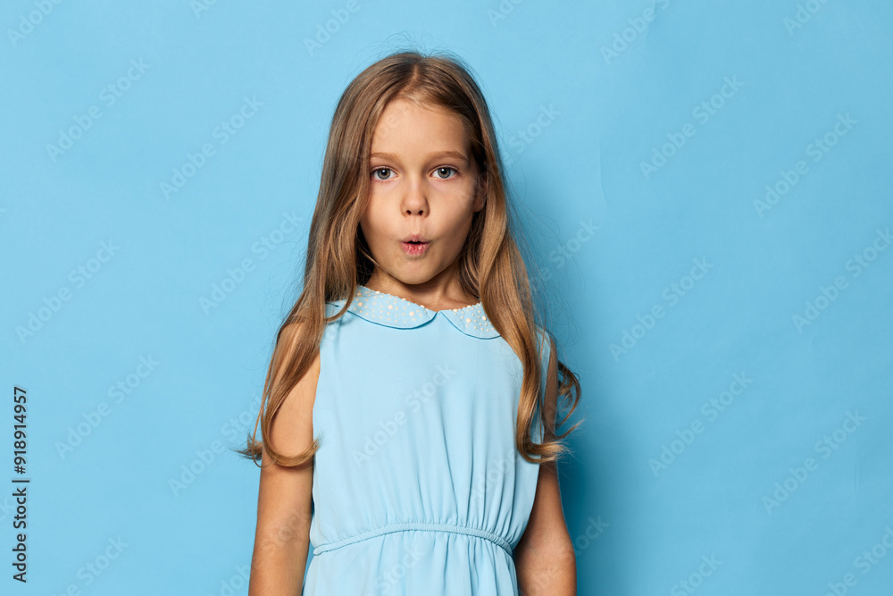 Cute little girl in blue dress making a funny face against a matching blue background Cute little girl in blue dress making a funny face against a matching blue background
