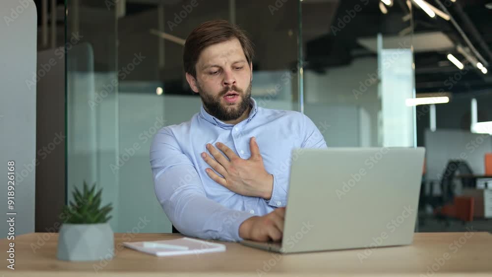 Worried businessman holding his chest in pain while working on his laptop at the office.