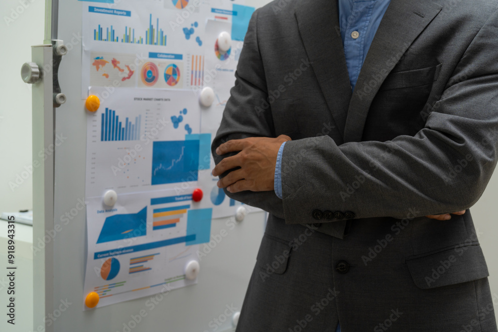 Fototapeta premium A male businessman explains graphs on a board during a meeting. He discusses marketing and finance strategies with the team, focusing on key data points to drive informed business decisions growth.