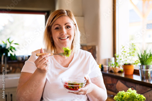 Portrait of beautiful young overweight woman choosing healthy food, eating vegetable salad. photo