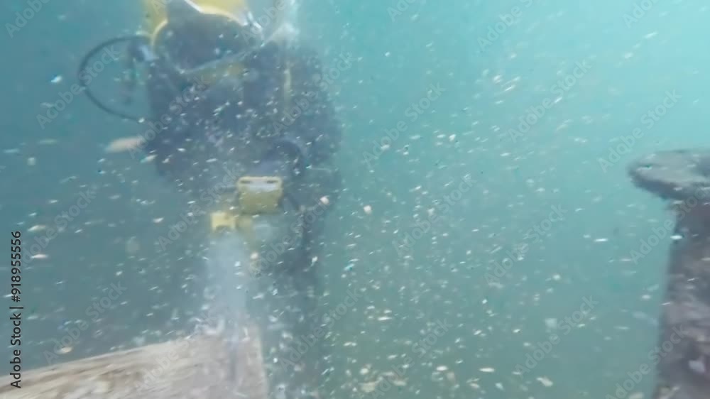 Commercial diver cutting log underwater with chainsaw