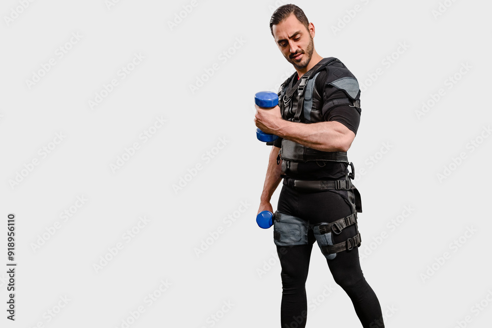 Strong man in EMS suit using electrical impulses to stimulate muscles while lifting dumbbells, Fitness regimen: Man engaged in electro stimulation training, perfect for workout routine visuals Strong man in EMS suit using electrical impulses to stimulate muscles while lifting dumbbells, Fitness regimen: Man engaged in electro stimulation training, perfect for workout routine visuals