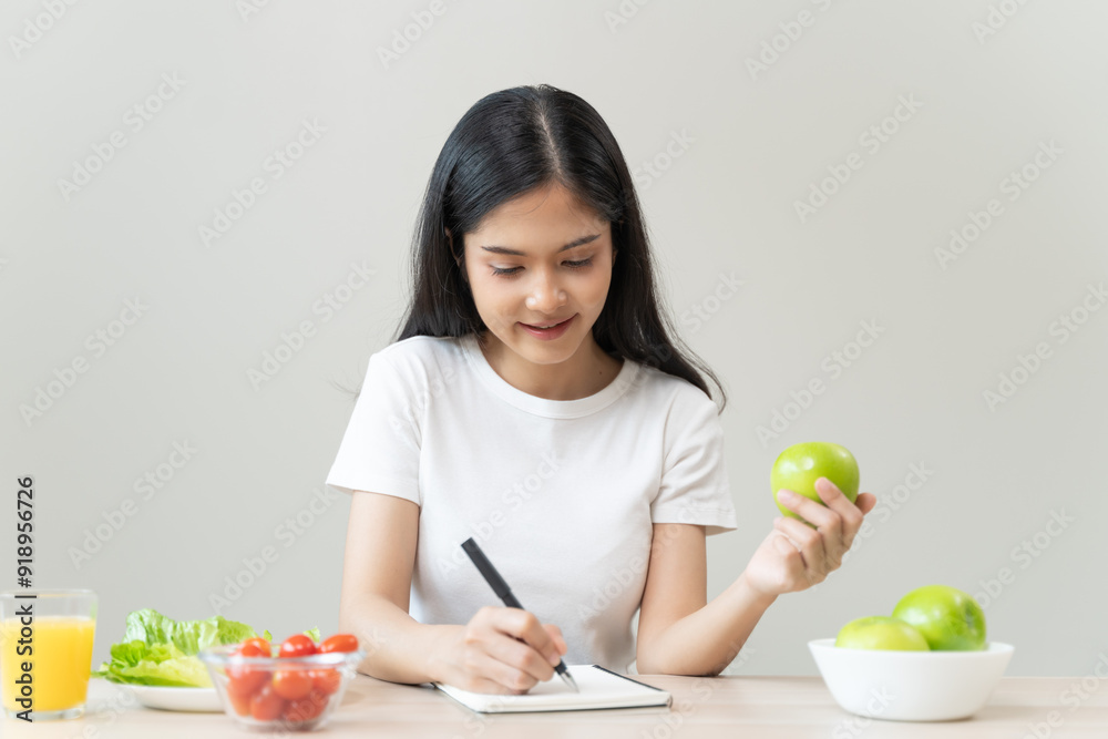 Asian beautiful woman i white t shirt writing note on the table and holding green apple with salad as breakfast. Asian beautiful woman i white t shirt writing note on the table and holding green apple with salad as breakfast.