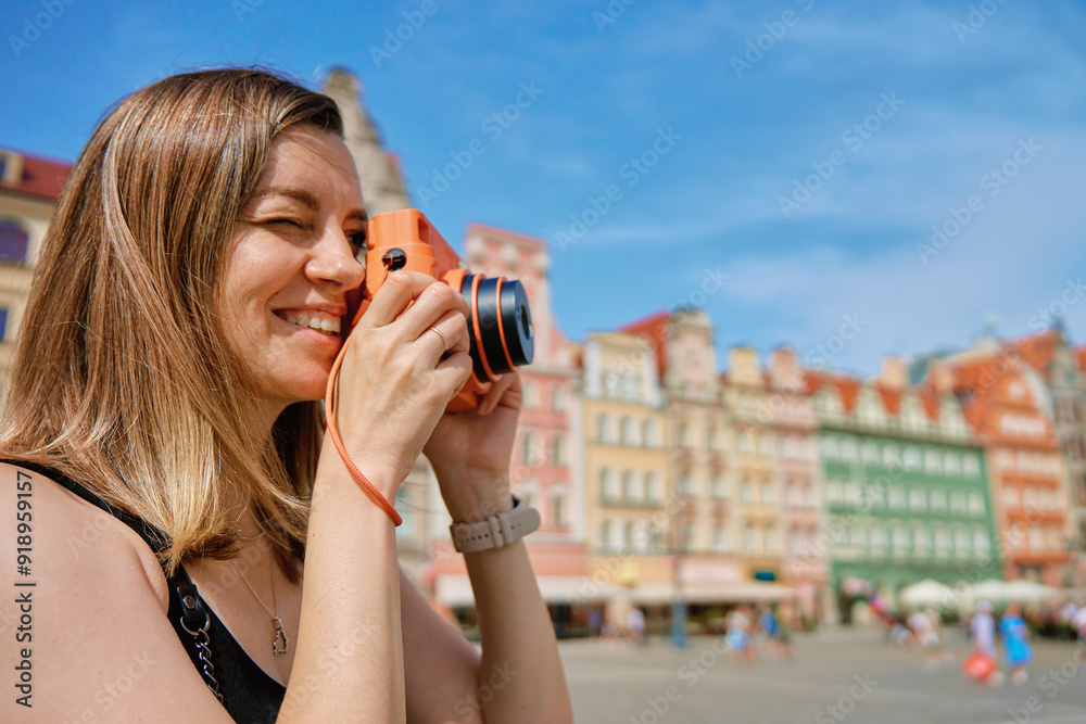 Woman taking photos in picturesque European city square, surrounded by colorful historic buildings. Female tourist captures memories during travel with vintage instant camera Woman taking photos in picturesque European city square, surrounded by colorful historic buildings. Female tourist captures memories during travel with vintage instant camera