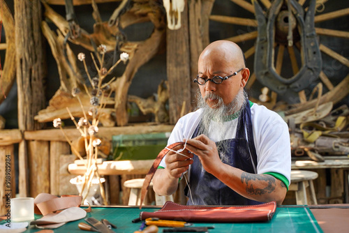 Closeup Asian leather craftsman is carefully to sew a leather belt for a customer in workshop., Leather craftsman concept.