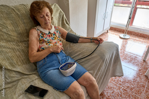  Senior woman measuring her blood pressure at home. Hispanic Senior Woman Measuring Blood Pressure at Home Using Digital Monitor for Healthcare and Wellness. photo