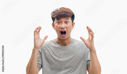 Young Asian man in gray t-shirt having a big surprise, isolated on gray background. The concept of the arrival of big luck. Shocked face