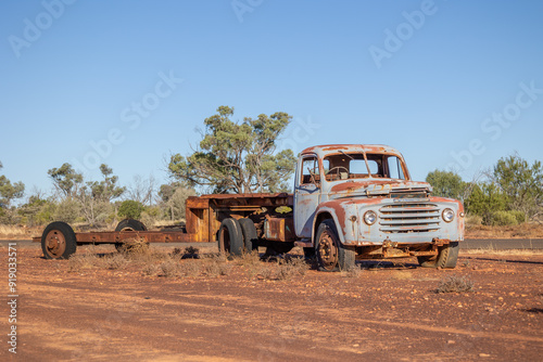 A rusted vintage truck and trailer, both having seen better days, stand as a monument to mining at the entrance to a tiny opal mining town in the outback country of Queensland, Australia. photo