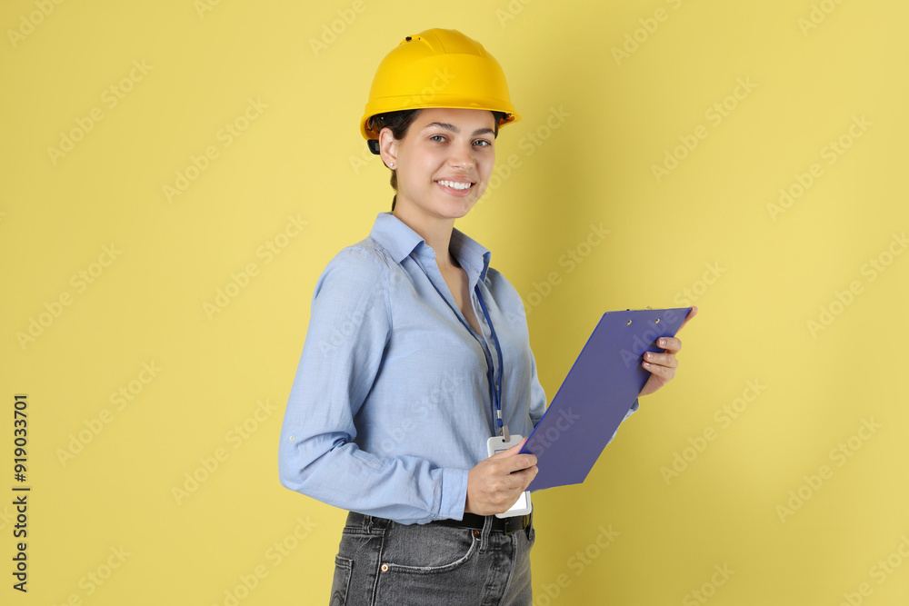 Engineer in hard hat with clipboard on yellow background Engineer in hard hat with clipboard on yellow background
