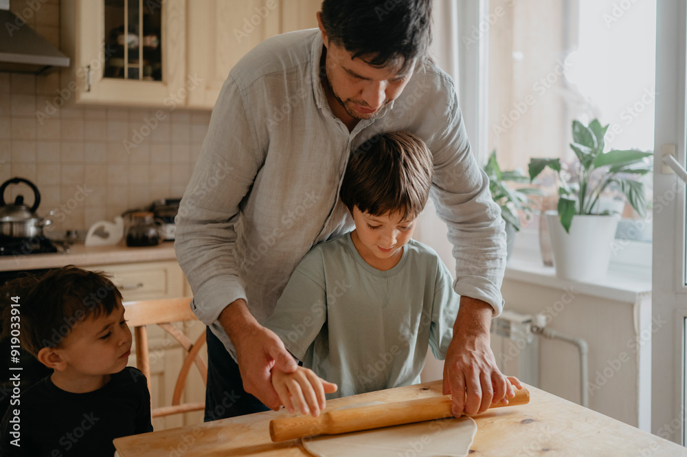 Father teaching son to roll dough in kitchen at home Father teaching son to roll dough in kitchen at home