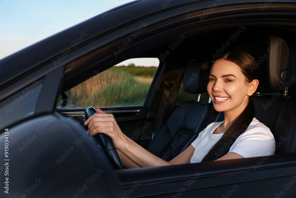 Smiling young woman holding steering wheel while driving car, view from outside