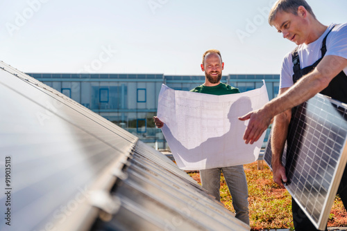 Craftsman and colleague installing a solar panel on the roof of a company building, planning for a sustainable future