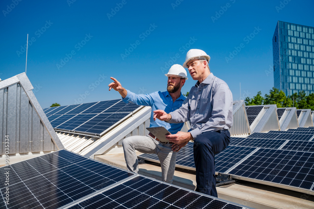 Two executives in hardhats discussing on the rooftop of a solar-powered corporate building Two executives in hardhats discussing on the rooftop of a solar-powered corporate building