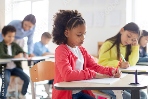 Diverse schoolchildren studying in classroom, sitting at desks and writing. Education, inclusivity, school and learning concept.