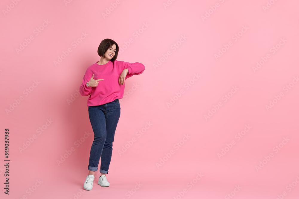 Smiling woman pointing at something on pink background. Space for text Smiling woman pointing at something on pink background. Space for text