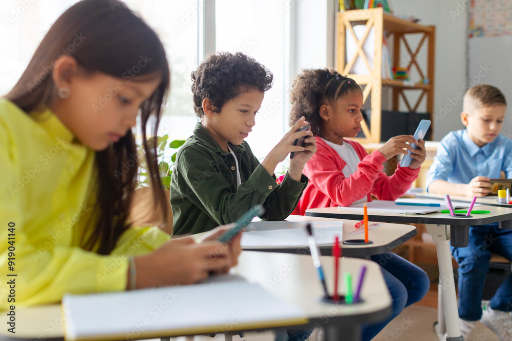 Diverse group of schoolkids using smartphones in classroom, having break during lessons, pupils holding phones and playing games Diverse group of schoolkids using smartphones in classroom, having break during lessons, pupils holding phones and playing games