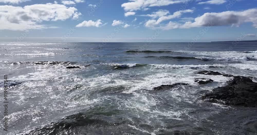 A wide shot of the ocean with a blue sky and white clouds shows the sun shining brightly on the sparkling water A wide shot of the ocean with a blue sky and white clouds shows the sun shining brightly on the sparkling water