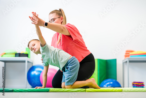 Young boy exercising with female physical therapist during therapy session. Child occupational physical therapy. Bilateral coordination.