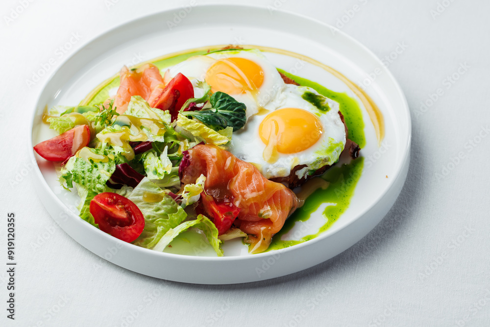Breakfast, two eggs served on toasted bread with a green herb sauce. Accompanied fresh salad, cherry tomatoes, and smoked salmon slices, all elegantly presented on a white plate and white background Breakfast, two eggs served on toasted bread with a green herb sauce. Accompanied fresh salad, cherry tomatoes, and smoked salmon slices, all elegantly presented on a white plate and white background