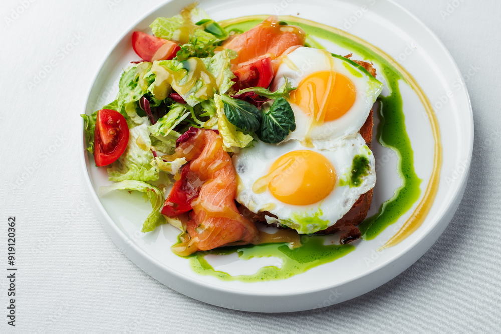 Breakfast, two eggs served on toasted bread with a green herb sauce. Accompanied fresh salad, cherry tomatoes, and smoked salmon slices, all elegantly presented on a white plate and white background Breakfast, two eggs served on toasted bread with a green herb sauce. Accompanied fresh salad, cherry tomatoes, and smoked salmon slices, all elegantly presented on a white plate and white background